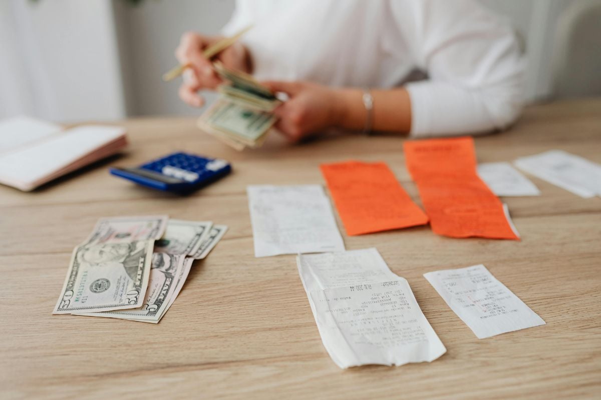 A person counting cash and calculating costs with receipts and dollar bills on the table 