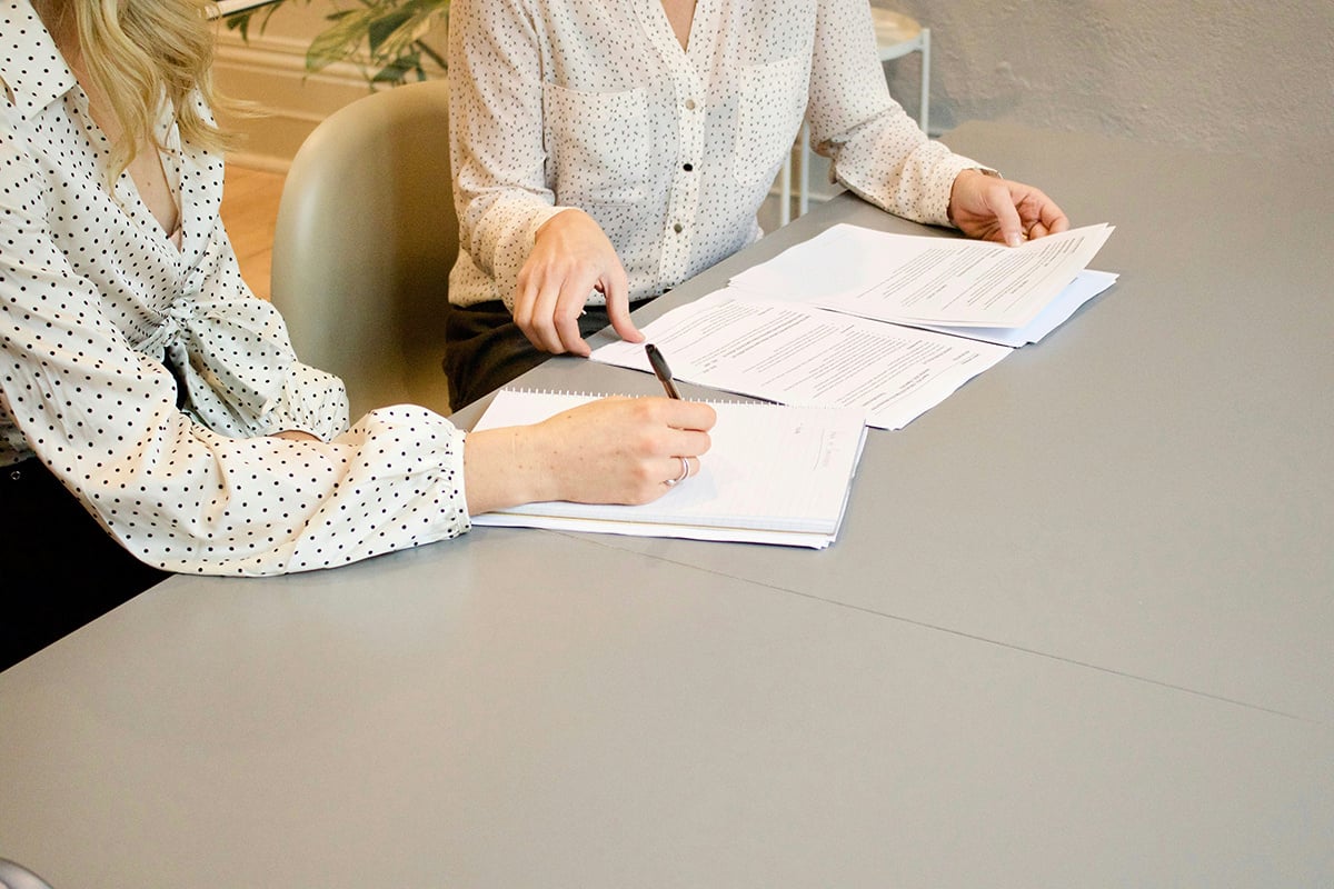 Two women filling out documents on a grey table