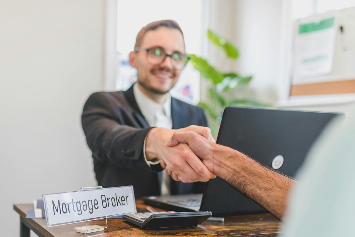 A friendly mortgage broker with glasses shaking hands with a client 