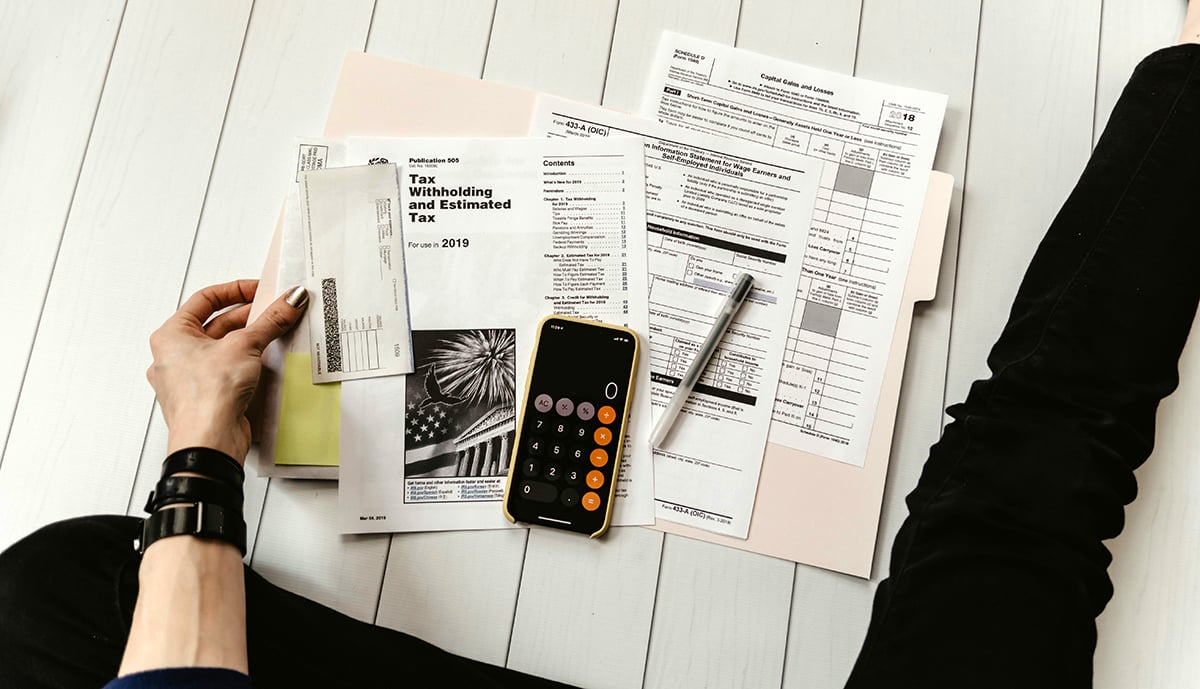 A person looking at a folder full of tax forms with a calculator and pen resting on top