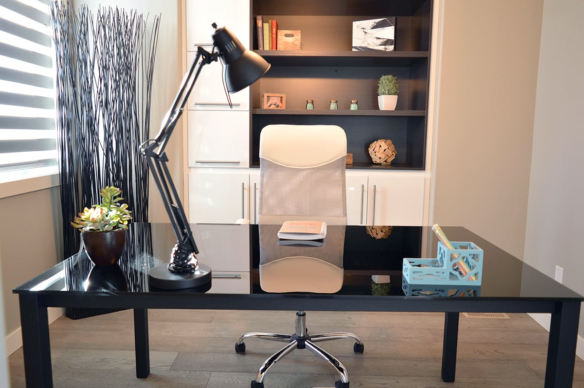 A modern looking home office with a desk, office chair lamp, bookshelf and other items