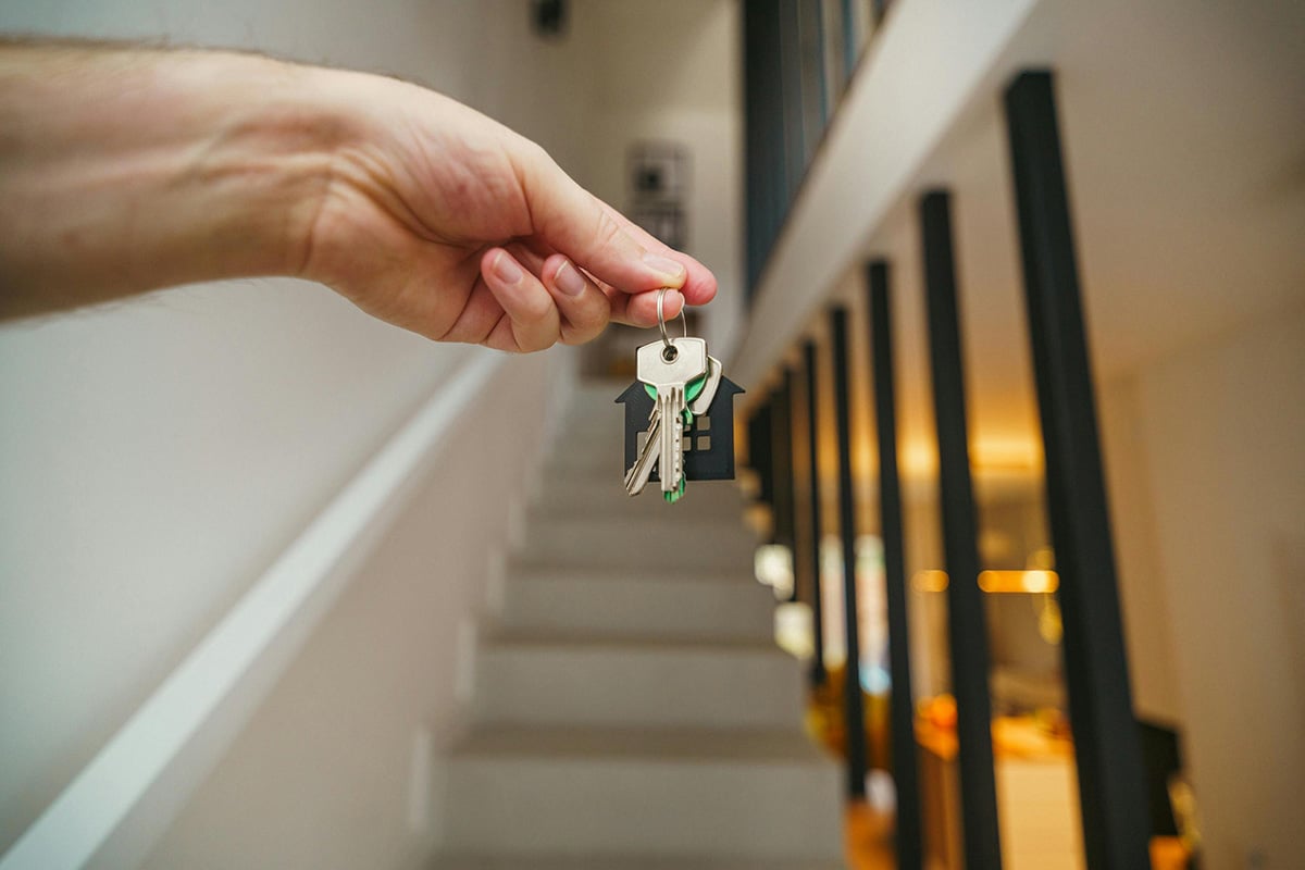 A person holding a set of keys in front of the staircase to a new home