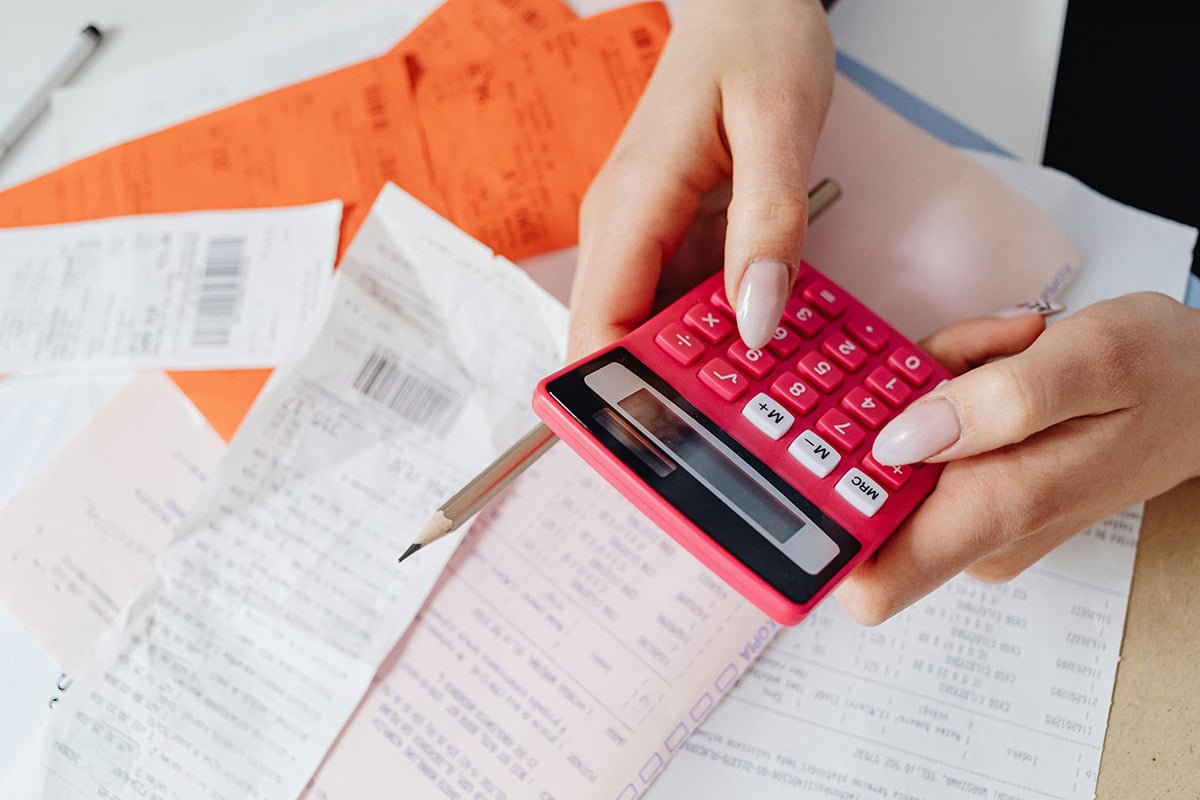 A person typing into a red calculator over a desk covered in receipts