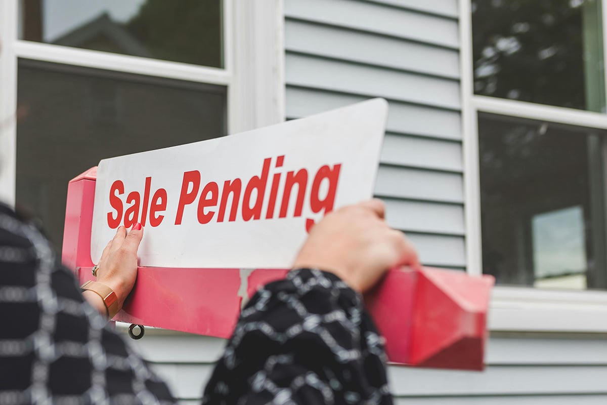 A real estate agent changing a for sale sign to sale pending after getting an offer